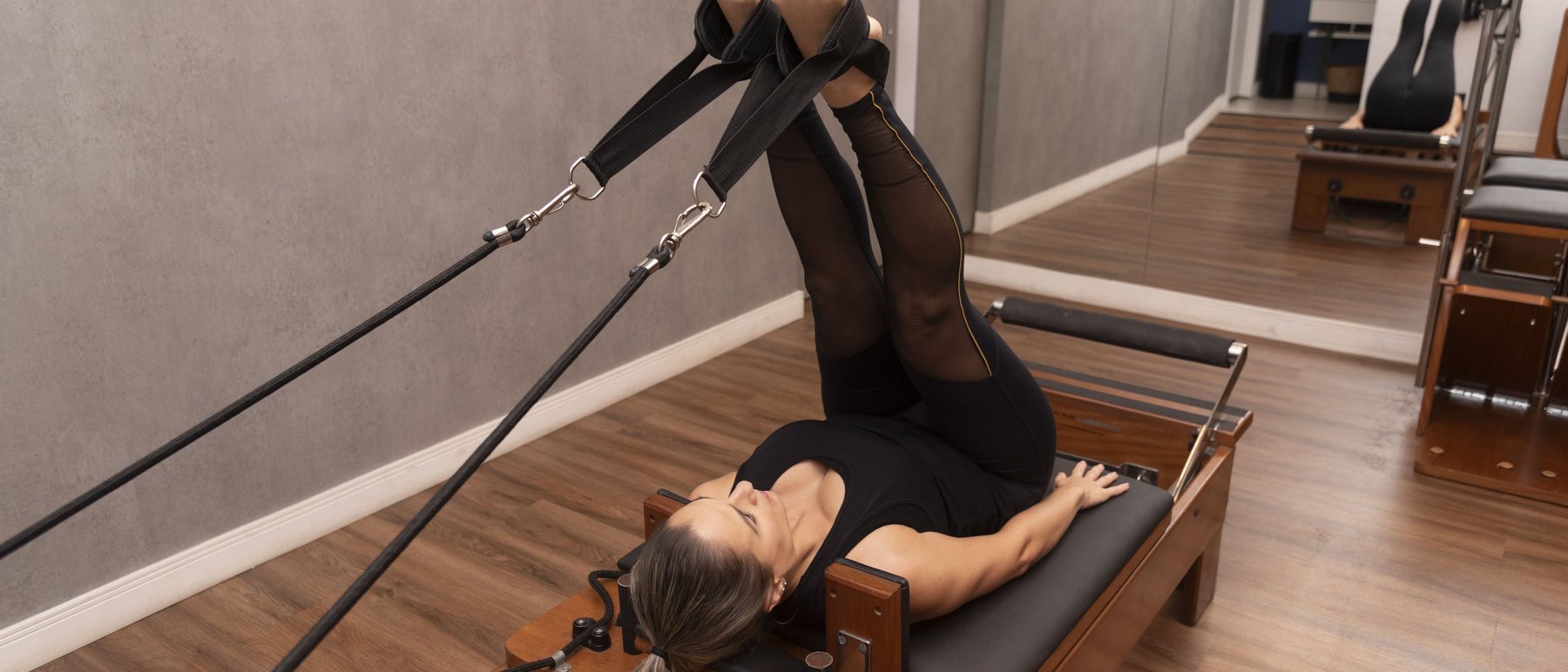 Aluna em exercício de alongamento no Reformer, no estúdio de pilates