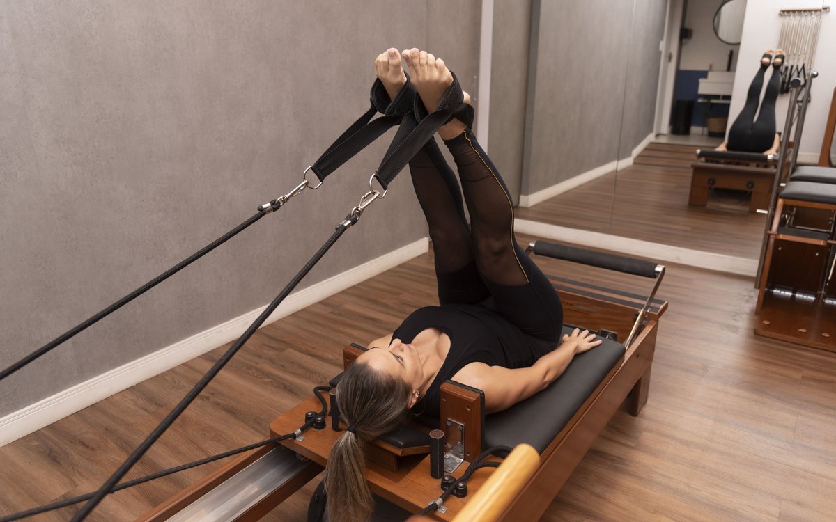 Aluna em exercício de alongamento no Reformer, no estúdio de pilates